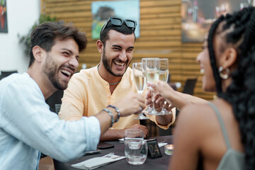 Happy diverse friends laughing and toasting with sparkling wine at an outdoor restaurant celebration.