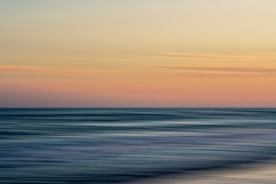 Blurred ocean waves blend into the soft pastel colors of a serene sunset.