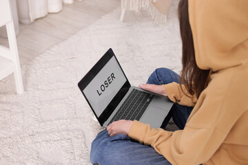 Cyber bullying. Upset teenage girl and laptop with text You Loser on floor indoors, closeup