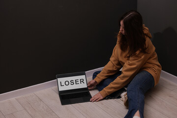 Cyber bullying. Upset teenage girl and laptop with text You Loser on floor indoors. Space for text