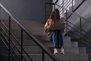 Cyber bullying. Upset teenage girl with laptop on stairs indoors. Space for text