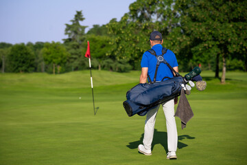 Golfer walking on the green carrying golf bag and clubs