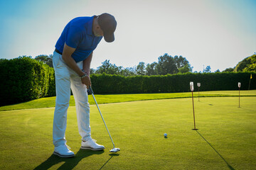 Mature golfer playing golf, putting on the green of a sunny golf course
