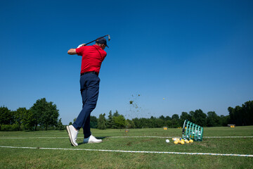 Golfer swinging golf club on driving range, hitting ball into the air