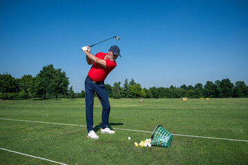 Golfer practicing swing on driving range with golf balls and basket