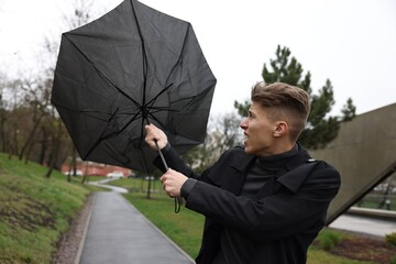 Man with broken umbrella fighting wind under rain outdoors
