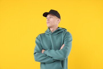 Young man wearing stylish black baseball hat on yellow background