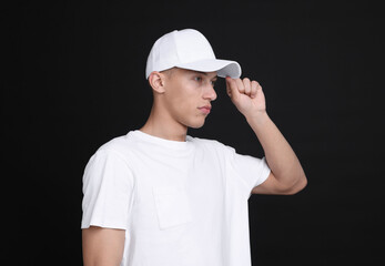 Young man wearing stylish white baseball hat on black background