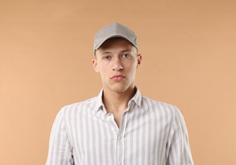 Young man in stylish baseball hat on beige background