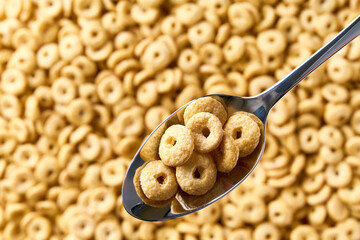 Whole grain cereal rings  in a metal spoon of above cereal loops as background. Copy space for text.