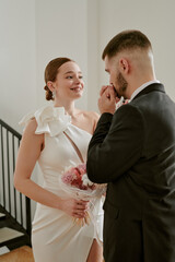Caucasian young adult woman smiling while holding bouquet, Caucasian young adult man in suit gently...