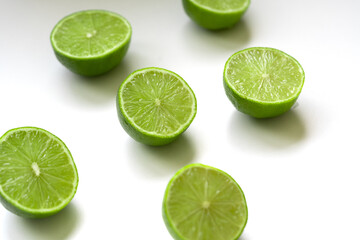 Vibrant green lime halves arranged on a clean white surface. The juicy texture and vivid color evoke a sense of freshness, summer, and natural simplicity. Selective focus.