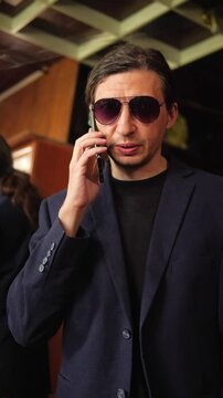 This footage conveys a cool and intriguing mood, depicting a person on a phone call while adjusting their sunglasses, suggesting a moment of discreet communication or a sophisticated persona