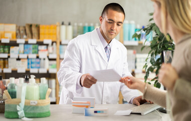 Fototapeta premium Polite young male pharmacist serving female client holding prescription in drugstore