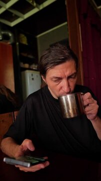A relaxed and connected mood is captured, ideal for depicting everyday routines, multitasking, or a quiet moment of enjoying a drink while engaging with a smartphone in a home setting