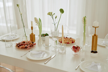 Wedding celebration table set with empty plates, crystal glasses, gold candlesticks, assorted appetizers and dessert arranged for guests