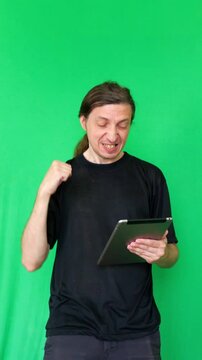 The man's enthusiastic reaction to his digital tablet creates an excited and triumphant mood. This shot is ideal for showcasing positive results, successful outcomes, or engaging digital experiences