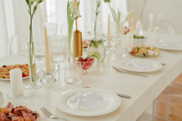 Wedding celebration table set with elegant glassware, plates, candles, floral arrangements and assorted appetizers, closeup showing place cards and festive food presentation