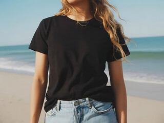A young woman in a black tshirt and light blue jeans stands on a beach