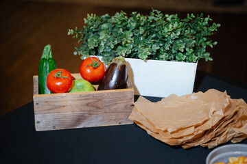 Wooden vegetable box, tray with herbs and craft paper on black table ready for making cold appetizers
