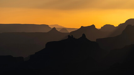 Silhouettes of mountains in the Grand Canyon at sunset, against a yellow sky.
