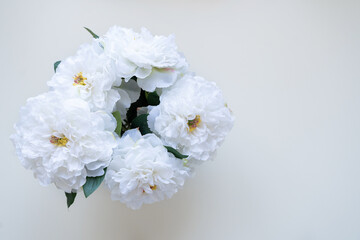 A beautiful bouquet of white artificial peonies stands on a windowsill in a transparent vase and looks like real flowers