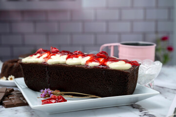 Rectangular and round chocolate pudding with cream on top and strawberries on a table with ingredients and pastry chef's hands decorating