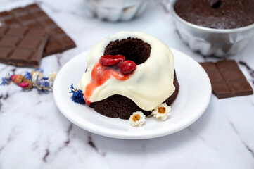 Rectangular and round chocolate pudding with cream on top and strawberries on a table with ingredients and pastry chef's hands decorating