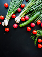 Bunch of fresh red cherry tomatoes, green leek, radish and cucumber on the black table background, top view of vegetables on the table.