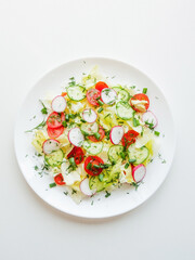Plate with fresh spring salad of sliced radish, cherry tomatoes, cucumber, greens and iceberg salad covered in olive oil, top view of plate with vitamin meal.