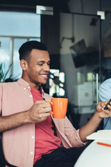 Multicultural male colleagues using modern technology during working time at office desktop connected to 4g wireless internet, smiling employee reading social news on content website via cellular