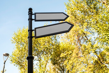 A signpost in a park with several empty arrows against a background of foliage.
