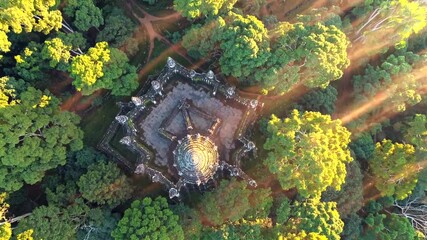 Drone view reveals golden dome temple beneath forest canopy, sunlight streaks highlight sacred structure, spiritual retreat blends into green harmony, evoking peace and mystery.