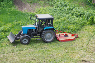 Obraz premium Professional lawn mower. The tractor is clearing the overgrown green grass.