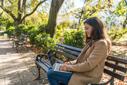 Professional occupation woman sitting on park bench, focused on laptop work blending outdoor relaxation with productivity showcasing modern remote working digital nomad lifestyle and urban tranquility