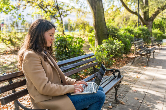 Professional occupation woman sitting on park bench, focused on laptop work blending outdoor relaxation with productivity showcasing modern remote working digital nomad lifestyle and urban tranquility