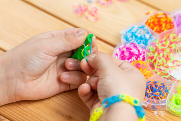 The child's hands weave accessories from colorful rubber bands. Children's hobby