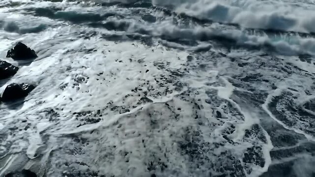 A wide bird&rsquo;s-eye view aerial video of powerful ocean waves crashing onto a dark, rugged shoreline.