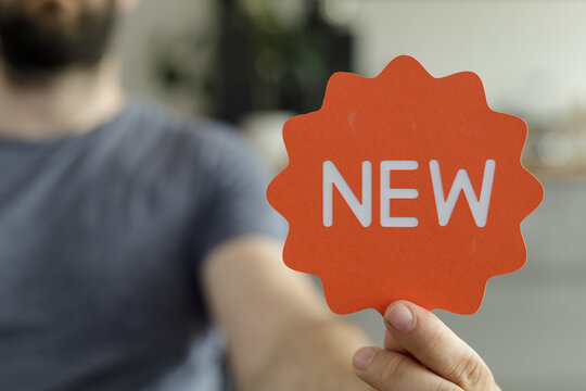 A man holds up an orange sign that says 'NEW'. Perfect for new product launches, announcements, and marketing.