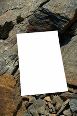 Mockup of white A4 sheet with shadows on large mountain stones in diffused sunlight. Layout of poster on stone background. White blank with space for text or design