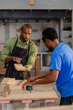 African American men working at woodshop bench, black apron, measuring plank using tape measure
