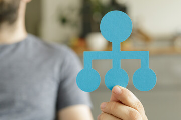 Person holding a blue paper organizational chart. Teamwork, hierarchy, management.
