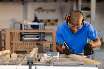 African American coworkers marking measurements on wooden plank at workshop table saw, copy space