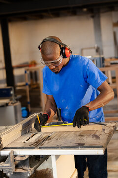 Wood plank resting on table saw undergoing precise measurement in busy carpentry workshop
