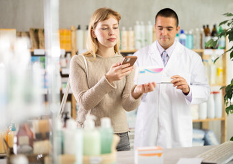 Young woman in a European pharmacy scans a package of headache pills with a mobile barcode, she reads detailed instructions online. Payment for goods by QR code