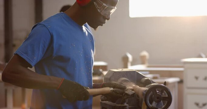 Operating African American coworkers shaping spindle on lathe in shop, with safety goggles, gloves