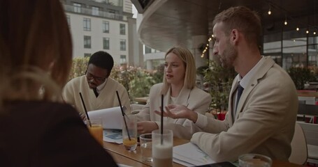 A diverse business team collaborates on a project at an outdoor cafe, reviewing documents and engaging in productive discussion. - Powered by Adobe