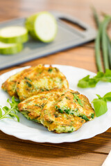 appetizing zucchini fritters with green onions in a plate on a wooden table