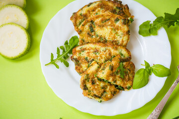 vegetable pancakes from zucchini with green onions in a plate on a green background