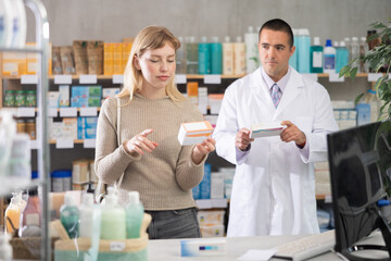 Fototapeta premium Girl studies composition of probiotic, buys product in drug store. Checking for absence of GMOs, age restrictions and recommendations for use. Man pharmacist in background offers similar product
